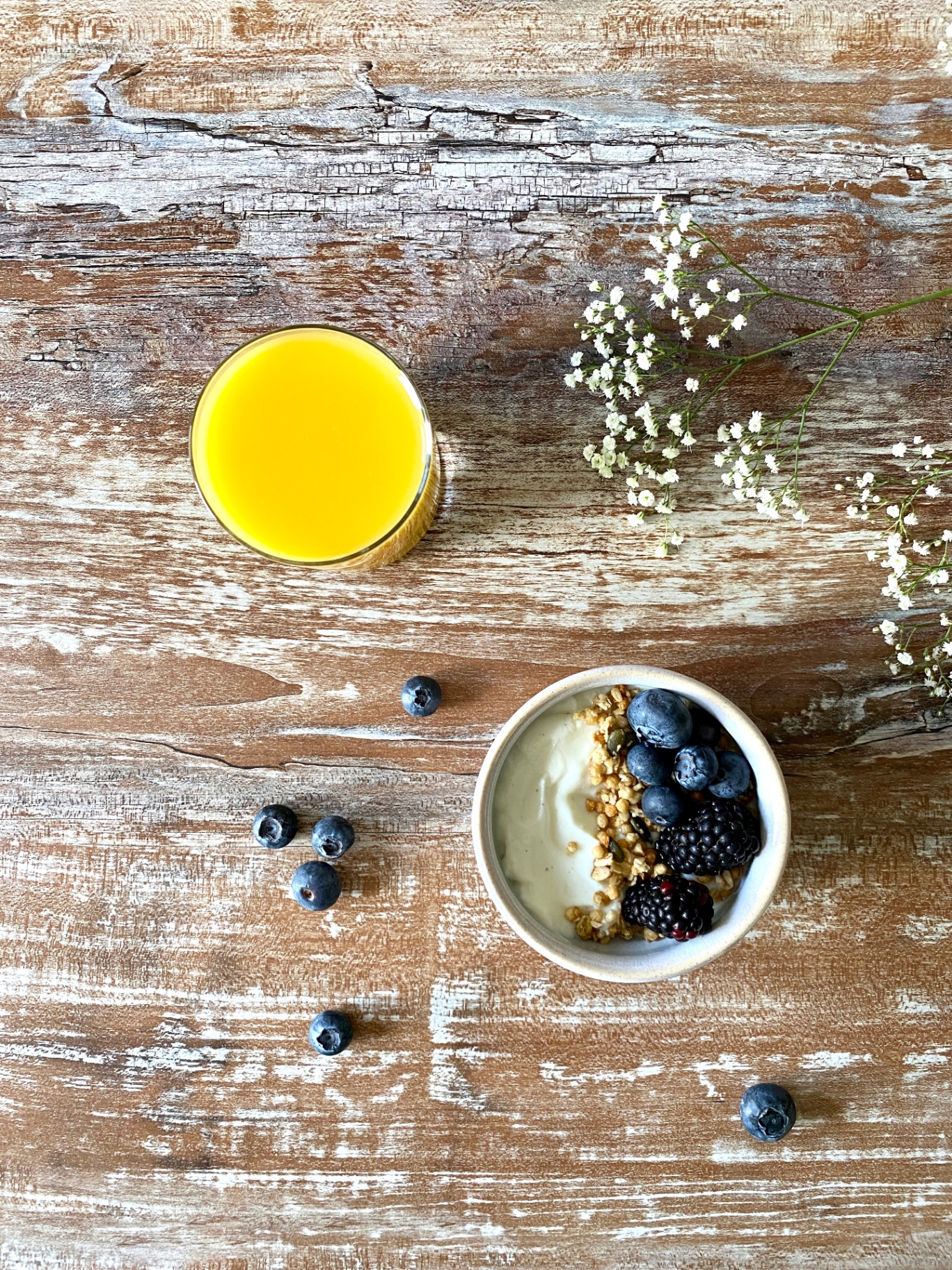 Fresh orange juice and a yogurt bowl with berries on a rustic wooden table