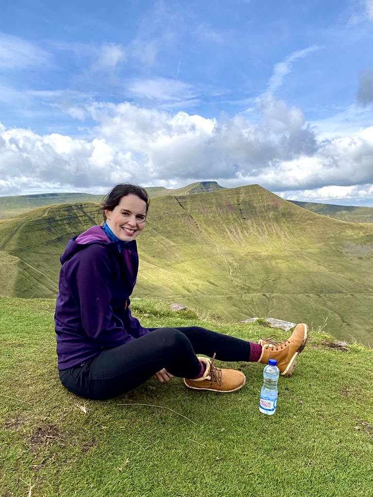 Rachel sitting on a grassy hilltop in the Brecon Beacons