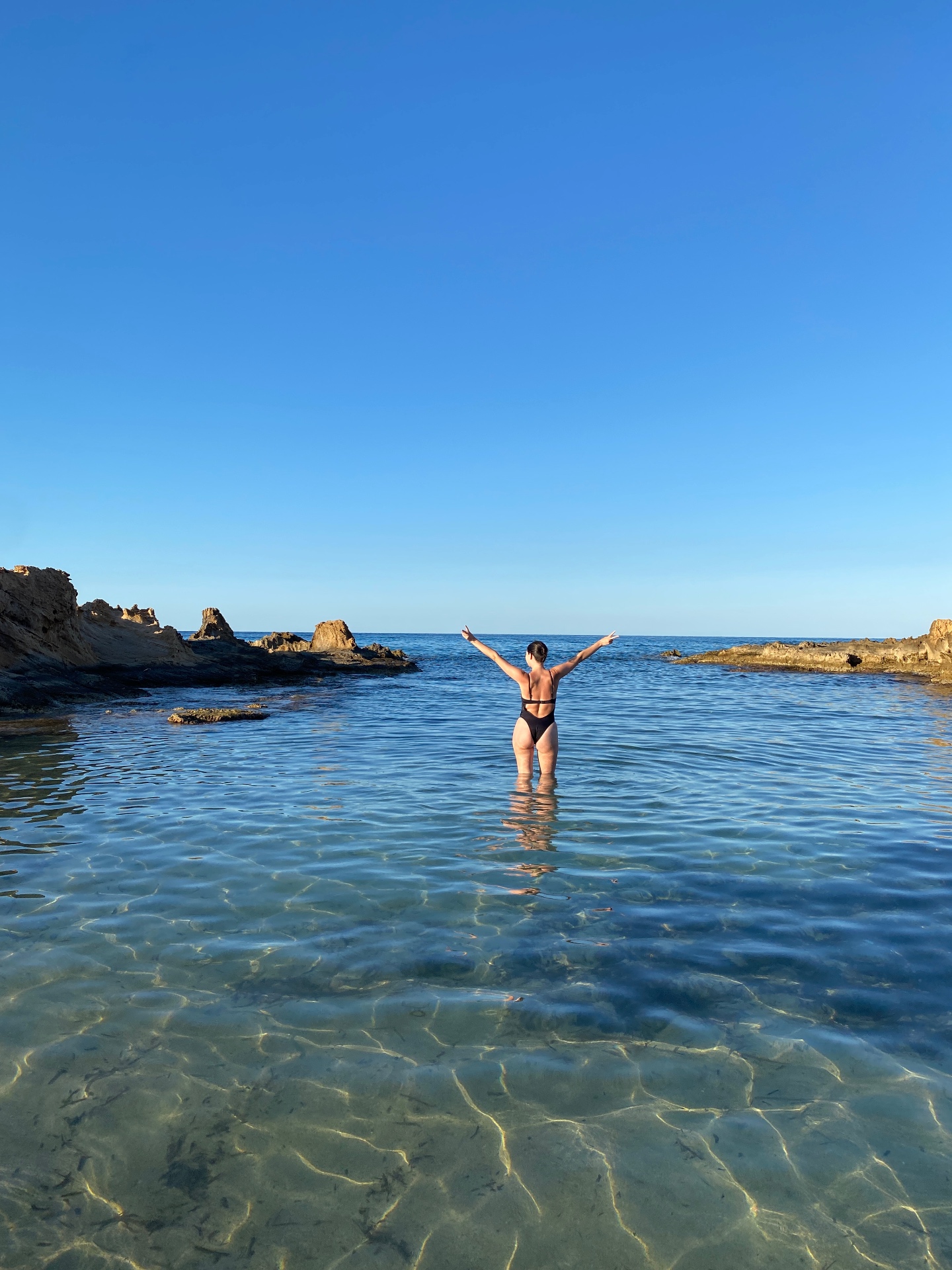 Rachel wading in clear blue sea with arms raised